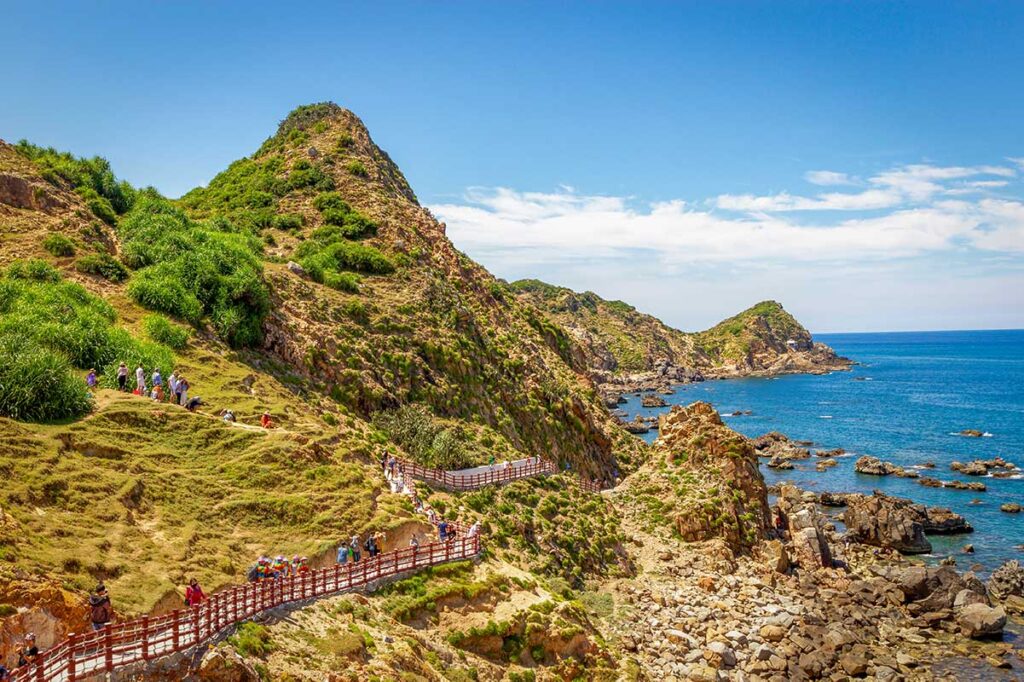 Tourists walking the red-railed coastal boardwalk along the cliffs at Eo Gió, Quy Nhon