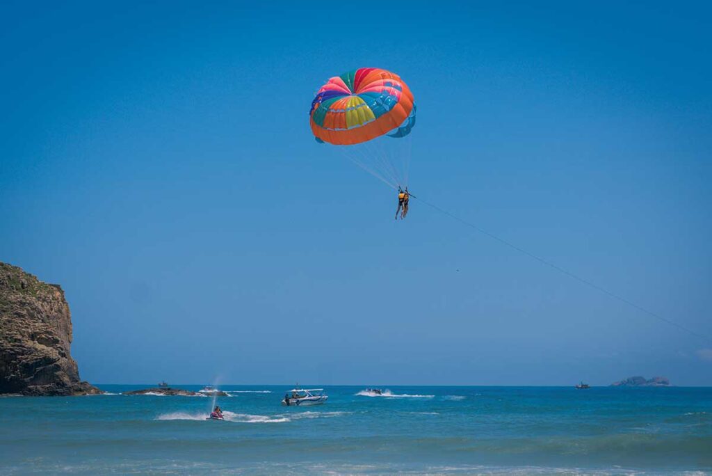 Parasailing over Ky Co Beach – Colorful parasail flying above turquoise waters at Ky Co Beach in Quy Nhon, with speedboats and jet skis in the background.