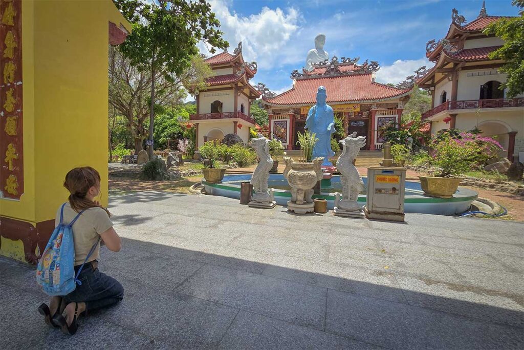 Traveler praying at the courtyard of Linh Phong Co Tu with the giant Buddha visible behind.