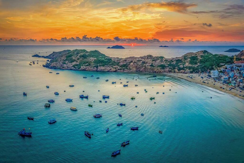 Aerial sunset over Nhon Ly fishing village and Eo Gió cliffs with colorful boats anchored in the bay