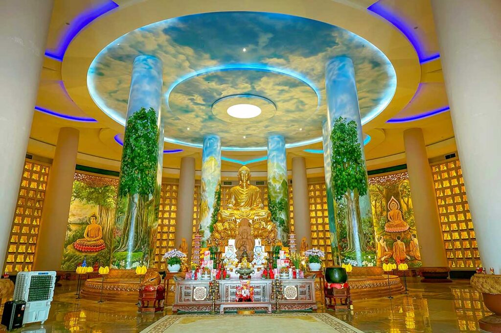 Interior of Ong Nui Temple Buddha hall with golden statue, murals, and hundreds of small Buddha icons.
