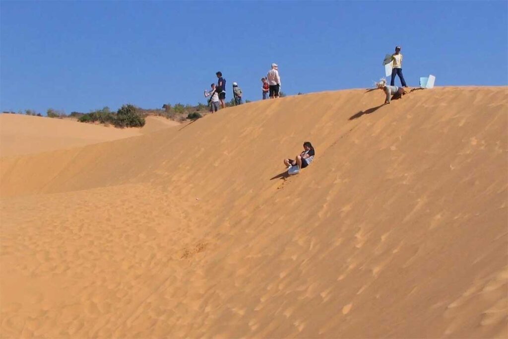 Visitors sandboarding down a steep slope at Phuong Mai Sand Dunes, enjoying one of the few adventurous activities available near Quy Nhon