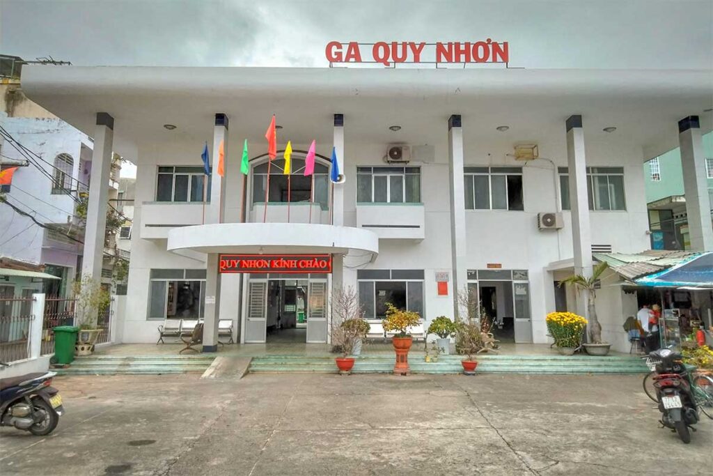 Front façade of Quy Nhon Railway Station with flags above the entrance, showing the modest city-center terminal in Binh Dinh Province.
