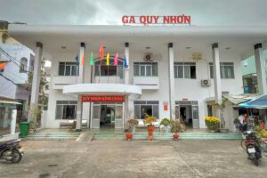 Front façade of Quy Nhon Railway Station with flags above the entrance, showing the modest city-center terminal in Binh Dinh Province.