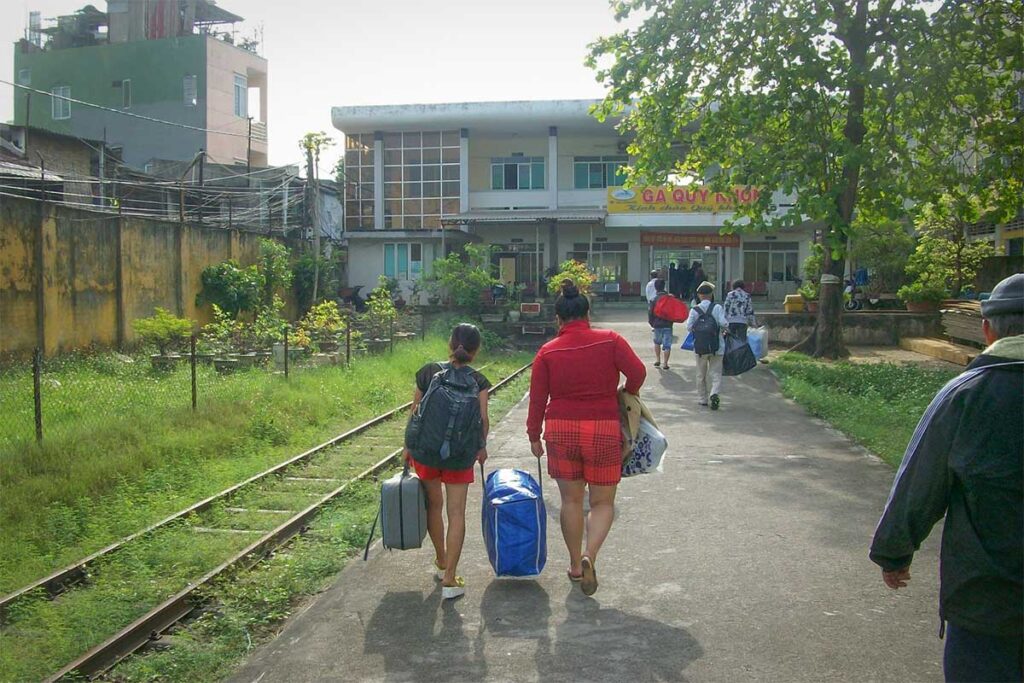 Travelers carrying luggage while walking along the tracks toward Quy Nhon Railway Station, illustrating the station’s small local character.