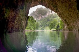Boat entering the Puong Cave entrance on Ba Be Lake, surrounded by limestone cliffs and lush forest during a Ba Be Lake tour in northern Vietnam.