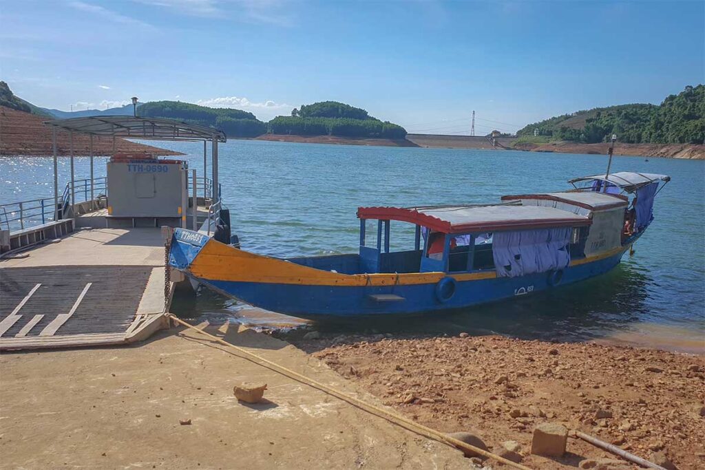 A small wooden boat and small ferry waiting to bring people to Bach Ma Zen Monastery on the other side of the lake