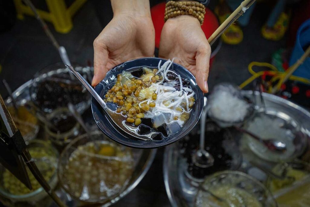 Traditional Hoi An chè sweet soup with beans, jelly, coconut milk, and shaved ice served at a street food stall.