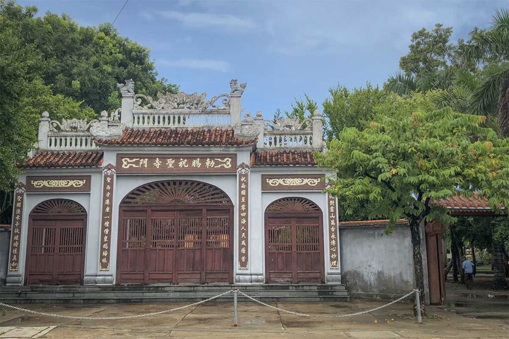 Main entrance of Chuc Thanh Pagoda Hoi An with wooden doors and decorative roof dragons – traditional Vietnamese temple architecture surrounded by lush greenery.