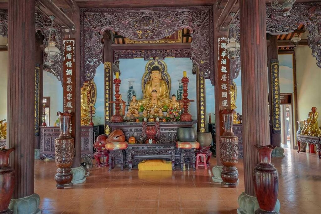Buddha altar inside Chuc Thanh Pagoda in Hoi An, detailed wooden carvings and golden statues