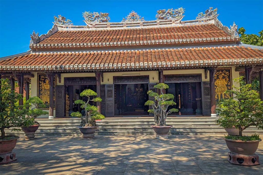 Front view of Chuc Thanh Pagoda Hoi An with traditional tiled roof and bonsai trees in ceramic pots