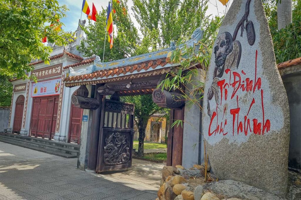 Entrance gate of Chuc Thanh Pagoda Hoi An with stone stele and Buddhist flags above tiled roof