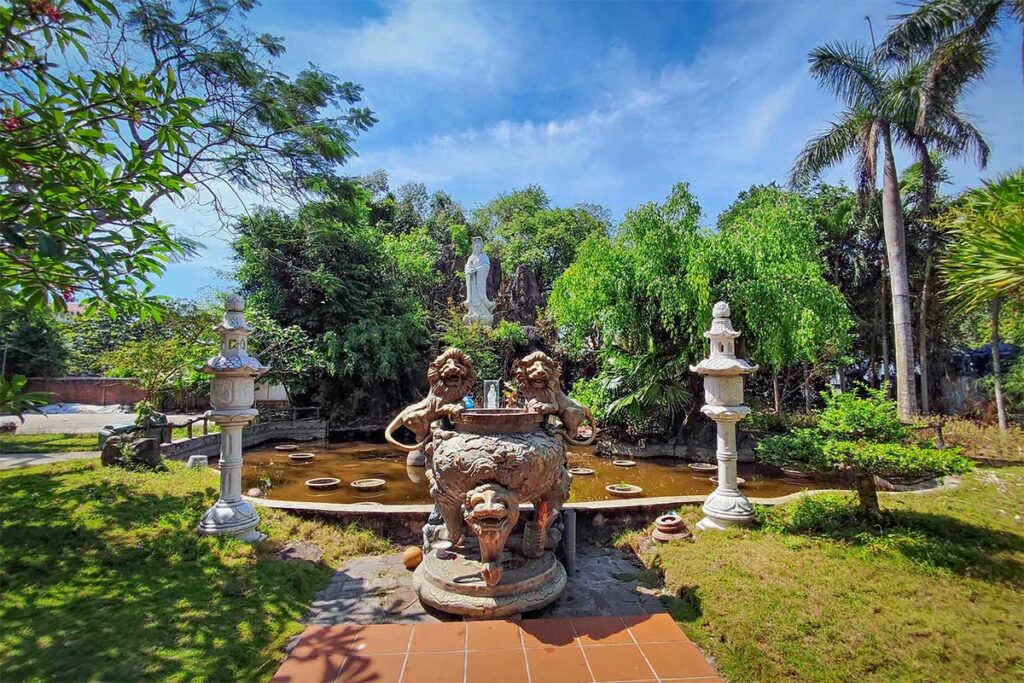 Stone incense burner and statues in front of lotus pond and tall Guanyin statue at Chuc Thanh Pagoda Hoi An