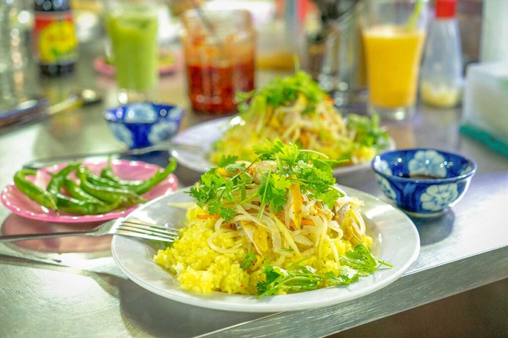 Plate of Hoi An’s famous chicken rice (cơm gà) with shredded chicken, fresh herbs, pickled vegetables, and green chilies served at a local eatery