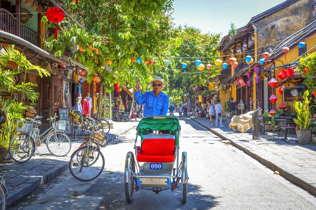 Cyclo driver posing on a lantern-lined street in Hoi An Ancient Town, capturing the relaxed atmosphere and traditional transport of the old quarter.