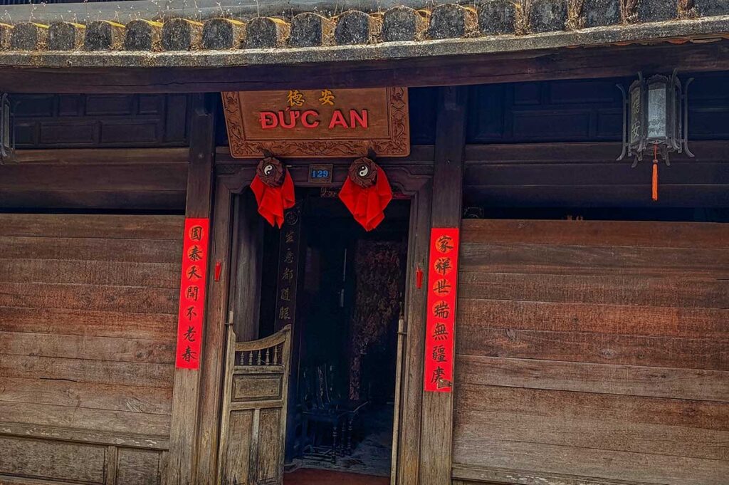 Front entrance of Duc An Old House in Hoi An with wooden doors, red Chinese calligraphy couplets, and traditional lanterns above the doorway.