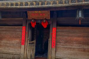 Front entrance of Duc An Old House in Hoi An with wooden doors, red Chinese calligraphy couplets, and traditional lanterns above the doorway.