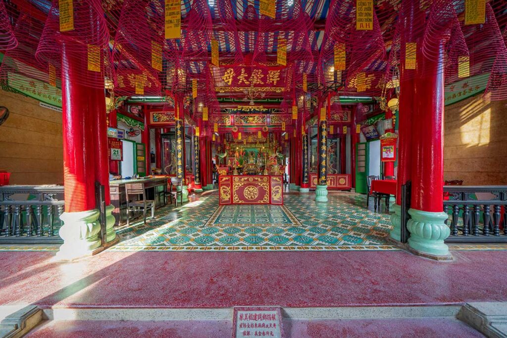 Interior of Fujian Assembly Hall in Hoi An, richly decorated with red pillars, golden inscriptions, and spiral incense coils.