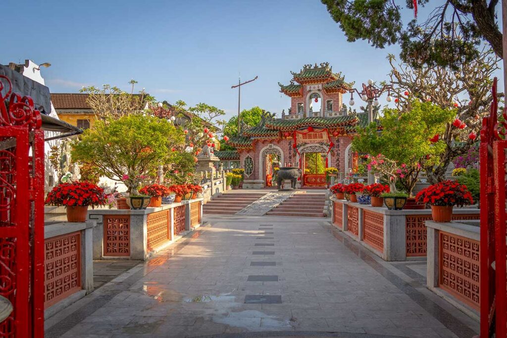 Main entrance gate of Phuc Kien Assembly Hall in Hoi An surrounded by bonsai trees and festive decorations.