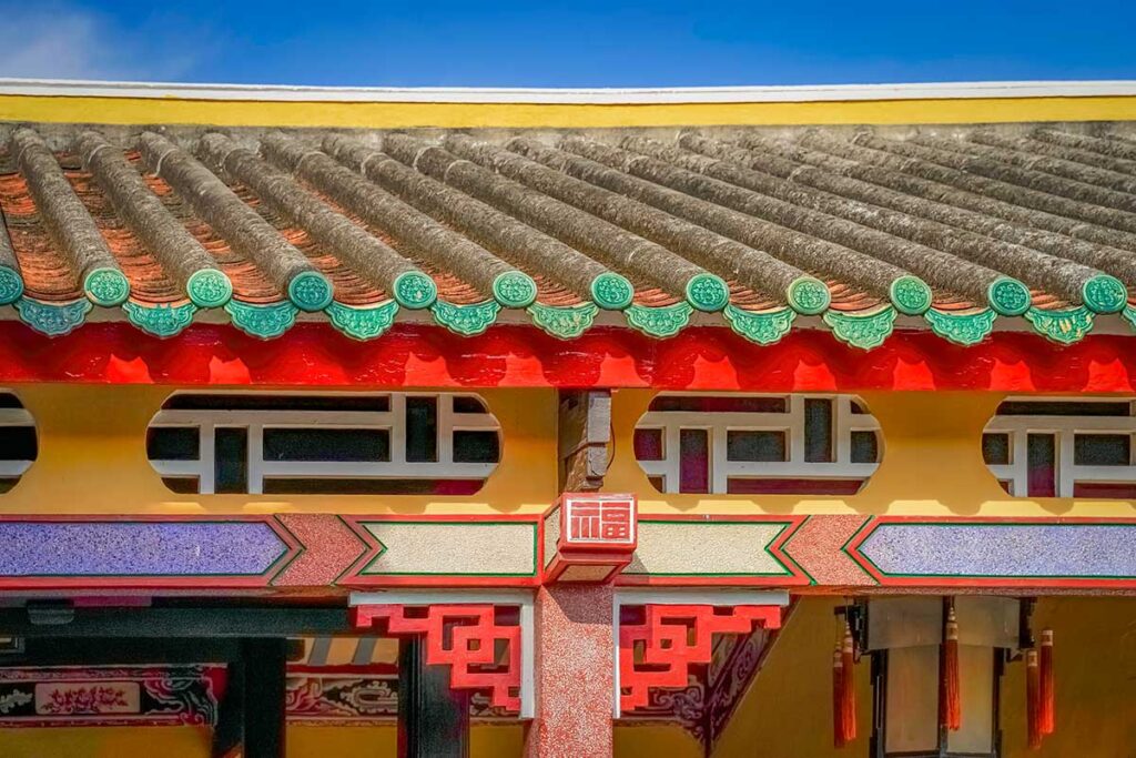 Decorative eaves of Hai Nam Assembly Hall—green ceramic ridge tiles, red bracketed beams, and classic Chinese motifs against a blue sky.