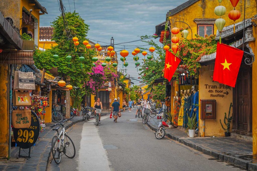 Colorful street scene in Hoi An Ancient Town with yellow merchant houses, lanterns, and Vietnamese flags creating a lively yet timeless atmosphere.