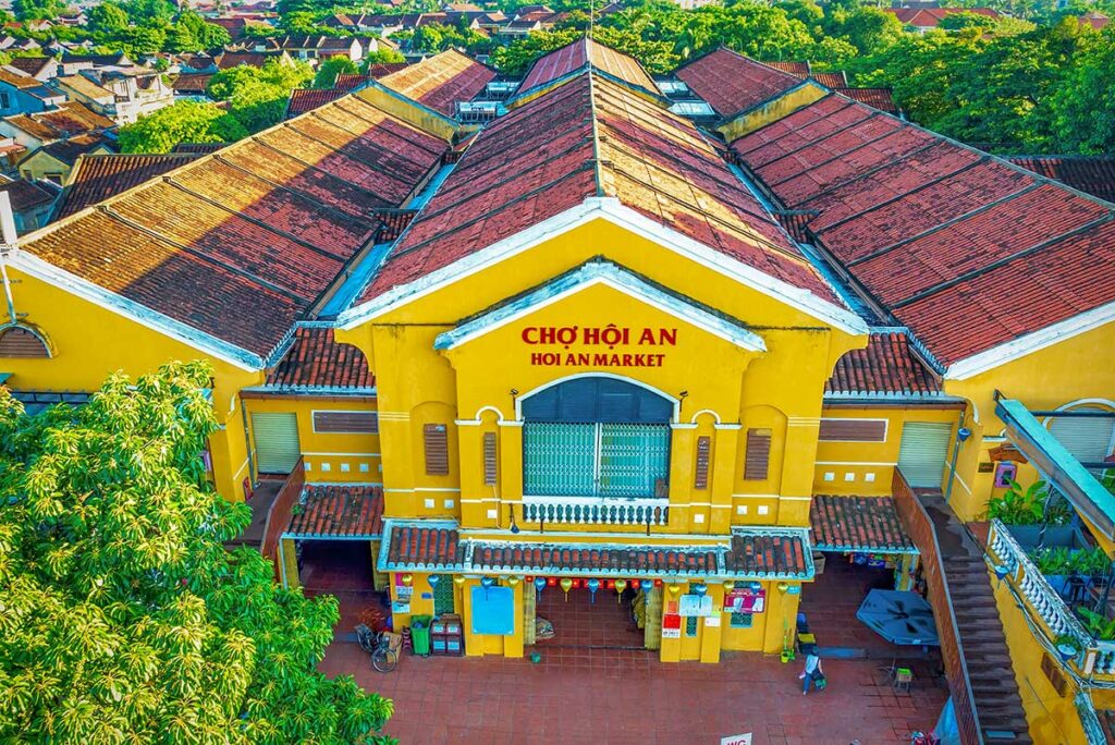 Aerial view of Hoi An Central Market building – Bright yellow facade and tiled rooftops of Hoi An Central Market, captured from above with the old town in the background.