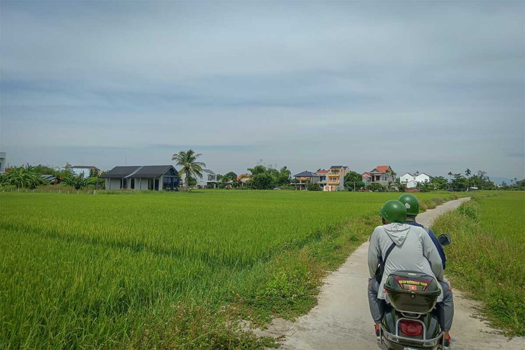 Two travelers on a motorbike exploring small village roads and rice fields – authentic countryside motorbike tour in Hoi An.
