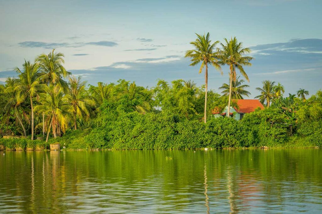 Tropical palms and riverside houses reflecting in the Thu Bon River – scenic boat ride through the countryside of Hoi An.