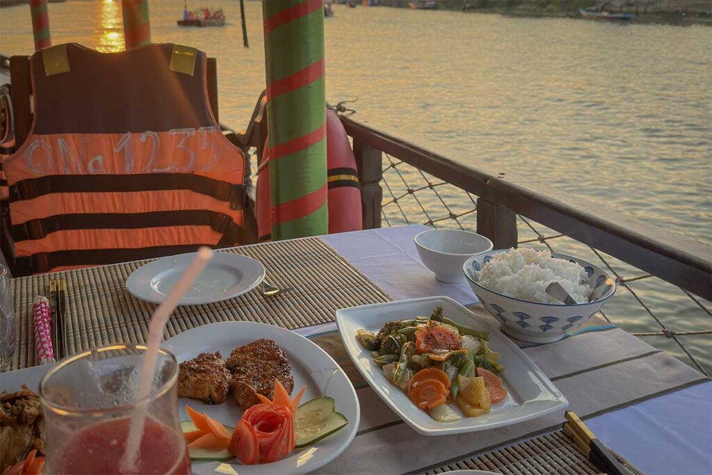 Table with Vietnamese dishes and river view on a peaceful dinner cruise – relaxing boat tour in Hoi An at sunset.