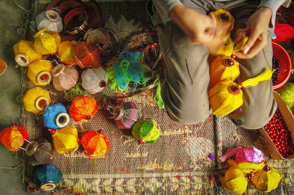 Close-up of traditional silk lantern making in Hoi An, with vibrant handmade lanterns in progress on a craftsman’s mat.