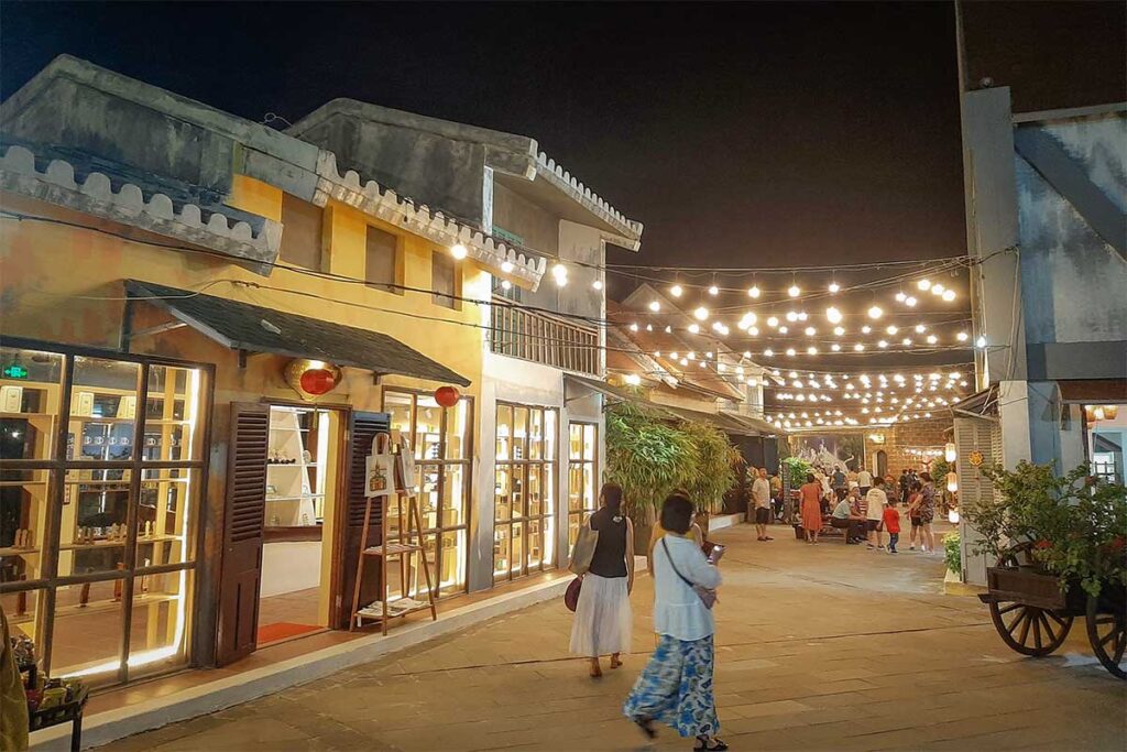 Shops and restaurants illuminated by string lights in the walking area of Hoi An Memories Land