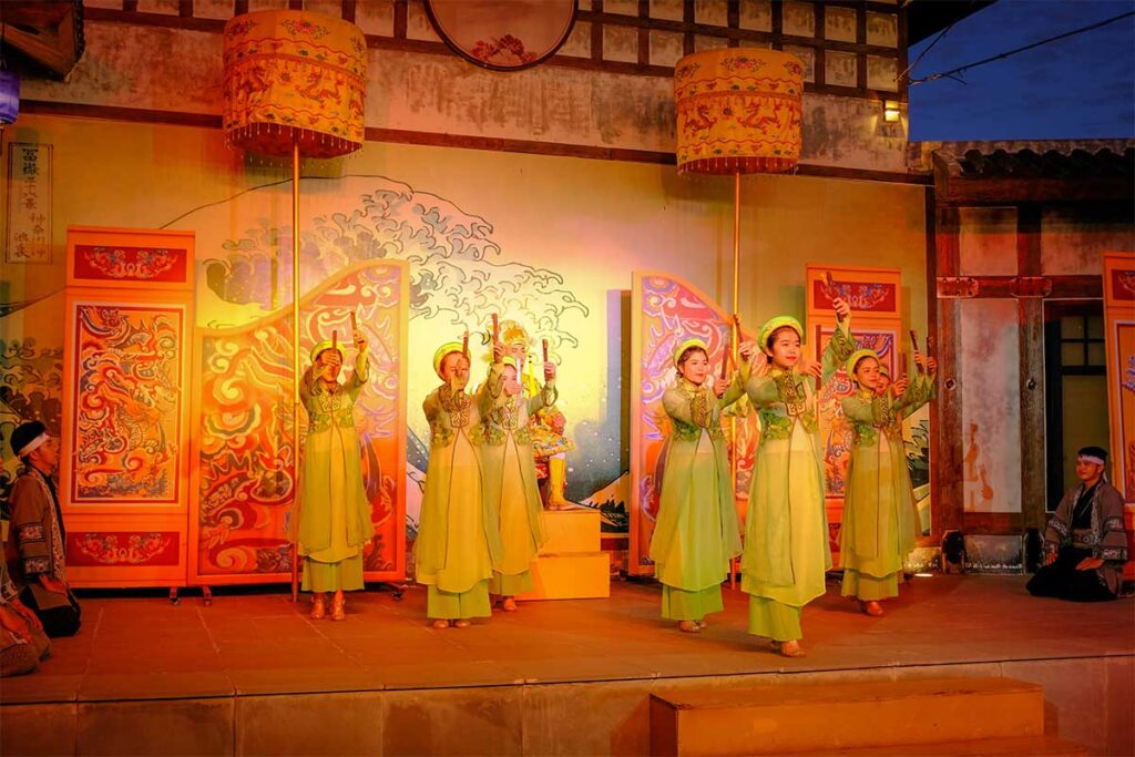 Group of dancers performing in ao dai costumes under colorful lights at Hoi An Memories Land.