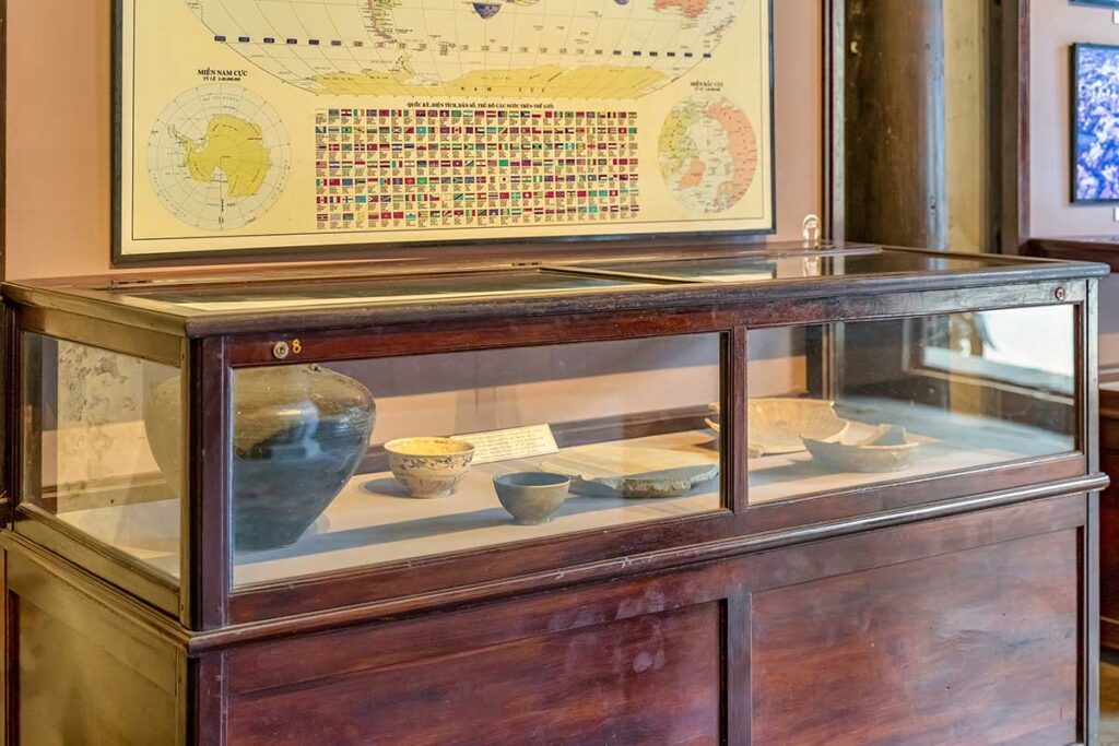 Showcase of archaeological artifacts and ceramic bowls at Hoi An Museum of Trade Ceramics – displayed beneath a world map tracing ancient maritime trade routes.
