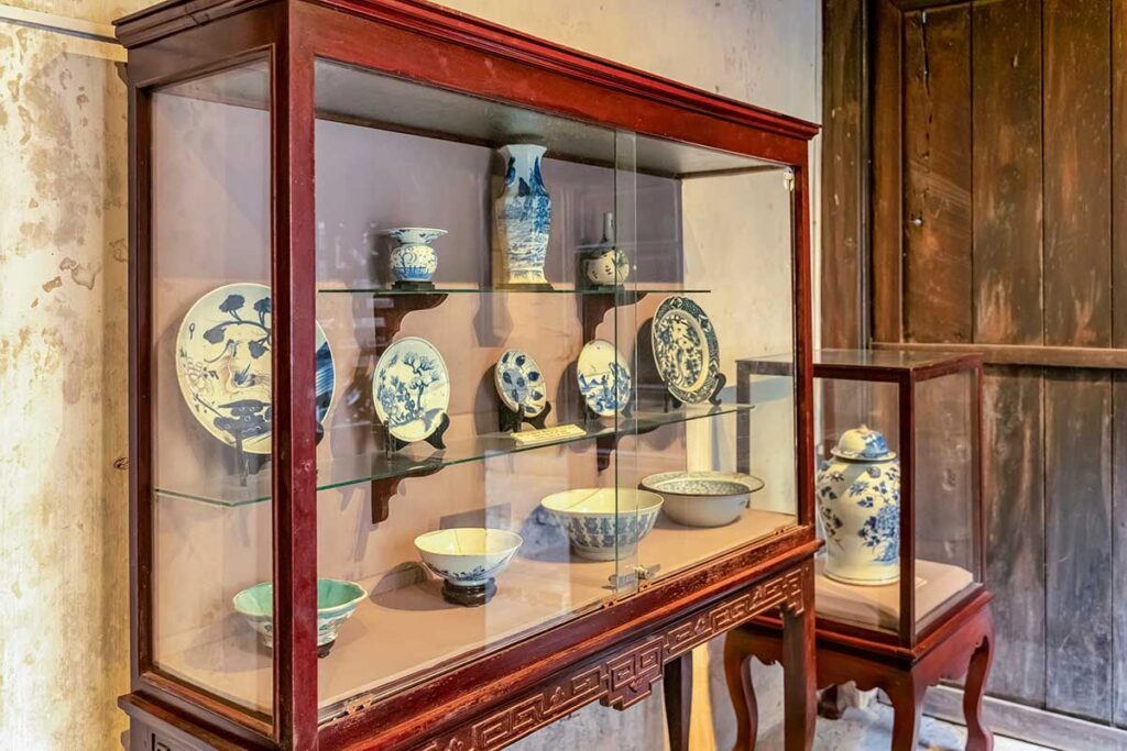 Exhibit of antique blue-and-white ceramics in wooden display cabinet at Hoi An Museum of Trade Ceramics – featuring porcelain bowls, vases, and plates from centuries of trade.