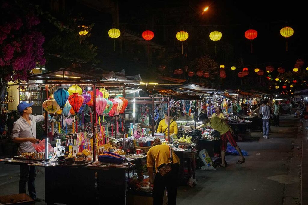 Vendors setting up colorful lantern stalls and souvenir stands at Hoi An Night Market after dark.