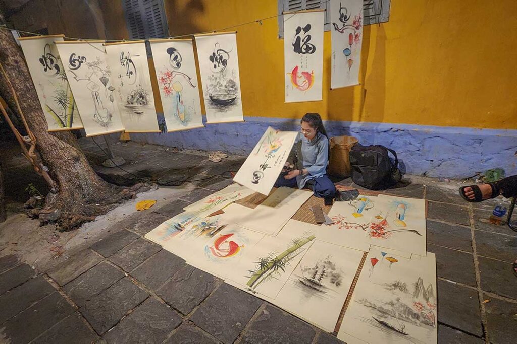 Local artist creating traditional calligraphy paintings on the street at Hoi An Night Market
