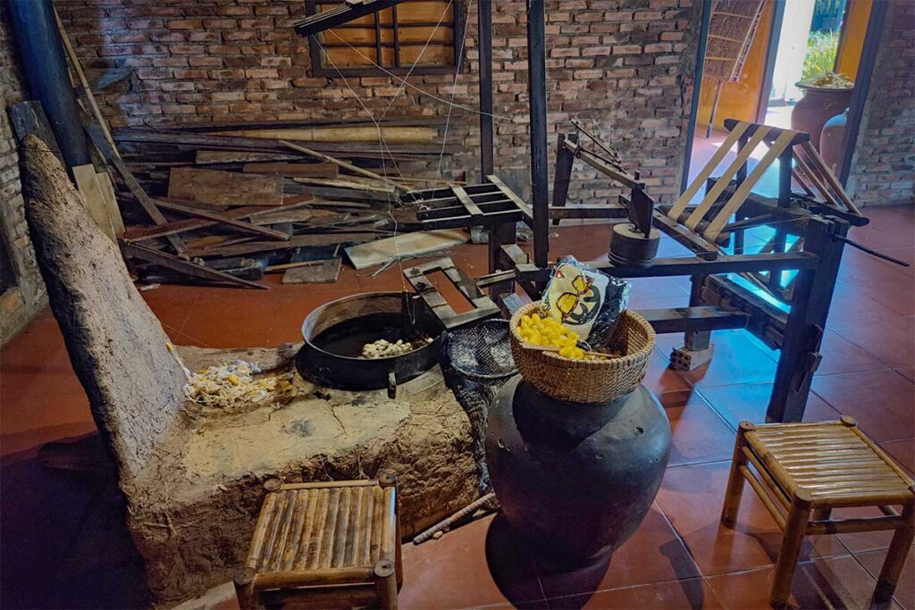 Ancient silk reeling equipment with cocoons and baskets on display in Hoi An Silk Village.