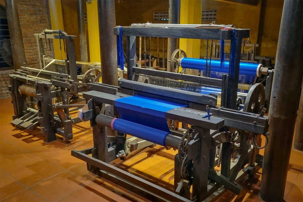 Traditional weaving looms with bright blue silk fabric inside Hoi An Silk Village.