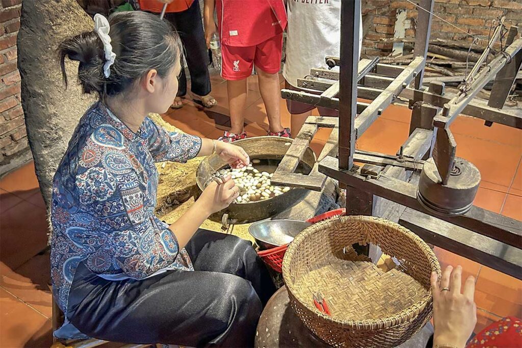 Woman reeling silk from boiled cocoons during a live demonstration at Hoi An Silk Village.