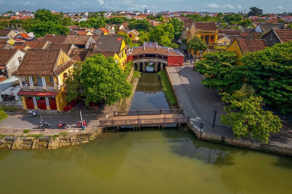 Japanese Covered Bridge in Hoi An from above – Aerial view of the iconic 16th-century Japanese Bridge surrounded by tiled-roof houses and the canal that runs through the UNESCO-listed old town.