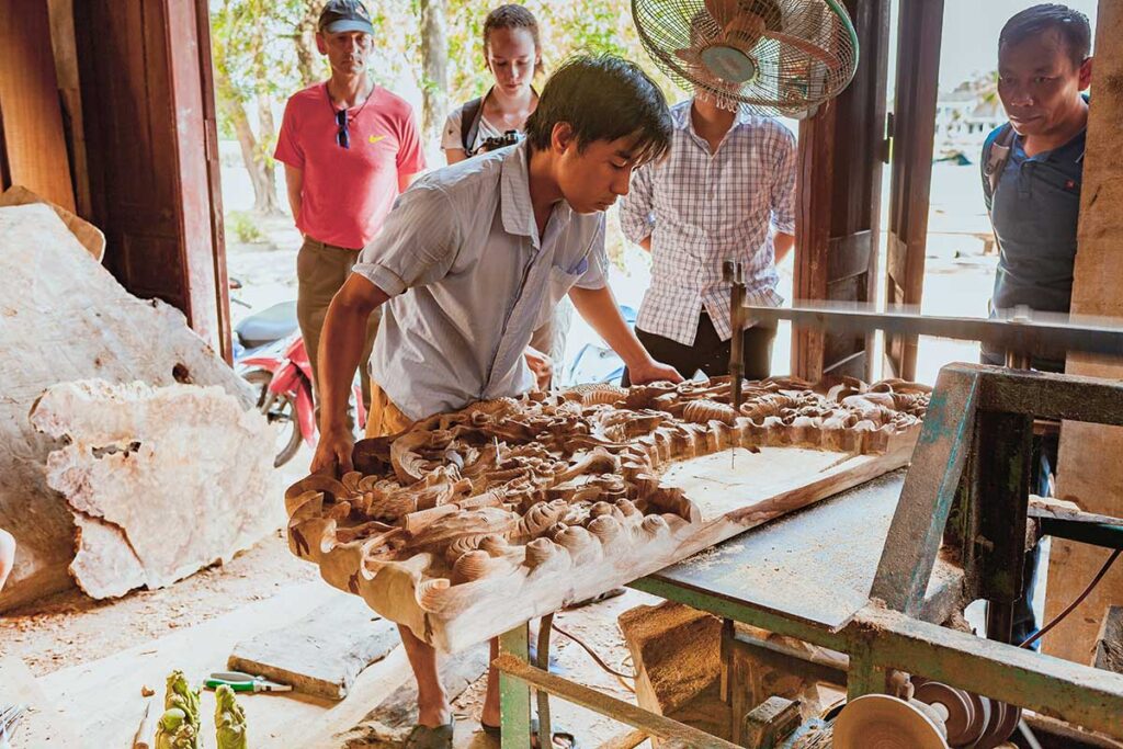 Local craftsman demonstrating intricate wood carving to visitors in Kim Bong Carpentry Village.