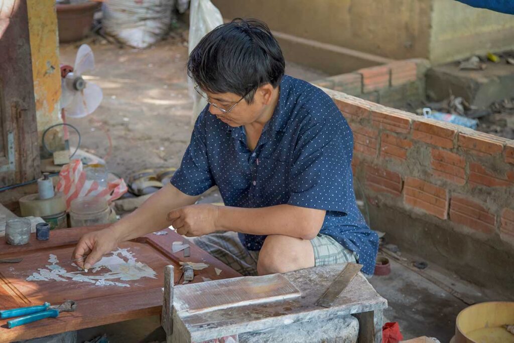 Artisan carefully inlaying mother-of-pearl into wood at Kim Bong Carpentry Village.