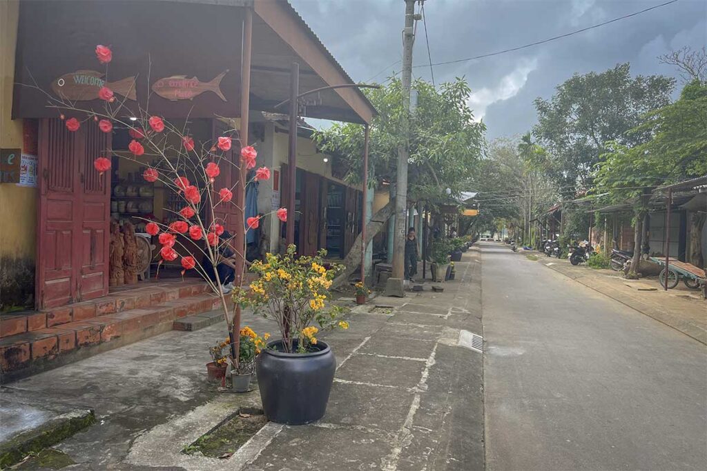 Quiet street in Kim Bong Carpentry Village – Peaceful street lined with workshops and flowering plants in Kim Bong Carpentry Village, Hoi An.
