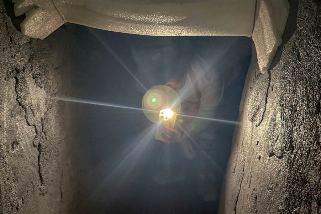 Visitor exploring the dark underground passage of Ky Anh Tunnels with a flashlight, experiencing the challenging conditions of wartime life.