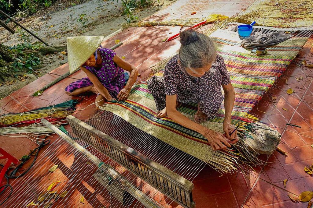 Elderly women weaving colorful sedge mats by hand near Ky Anh Tunnels, preserving traditional craft culture in Quang Nam.