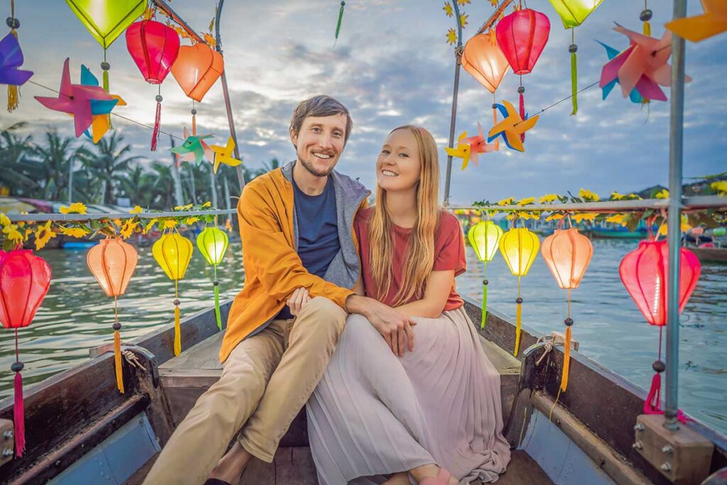 Couple enjoying a lantern-lit river cruise in the old town – romantic evening boat ride in Hoi An.