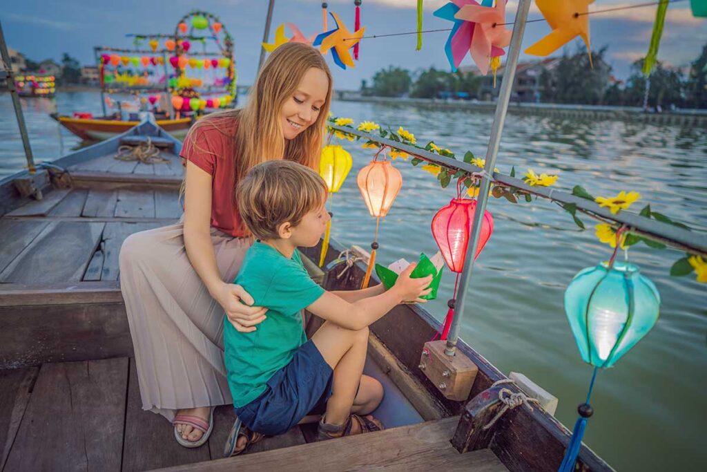 Family lighting paper lanterns on a river boat – magical lantern boat tour in Hoi An for visitors with kids.