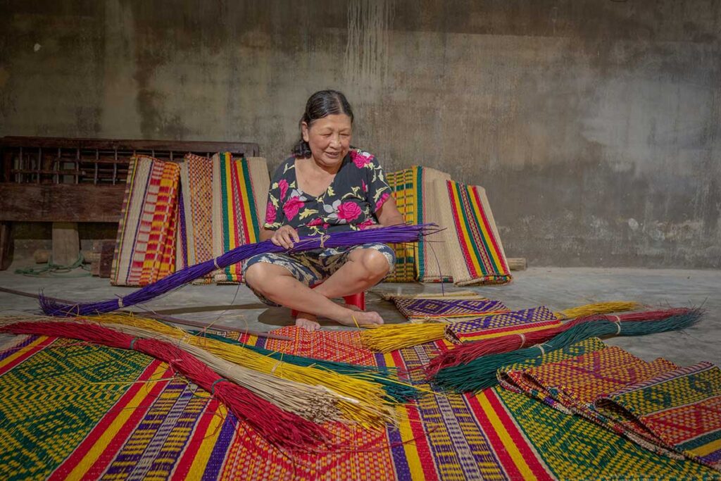 Local woman weaving colorful sedge mats by hand in a traditional mat weaving village near Tam Ky, Quang Nam.