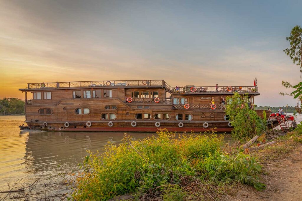 Mekong Eyes Classic wooden cruise boat docked along the Mekong Delta at sunset