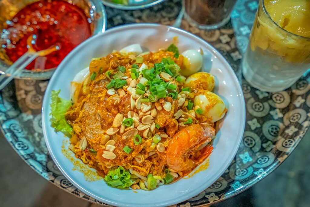 Traditional Mi Quang noodles in Hoi An with shrimp, pork, quail eggs, peanuts, and fresh herbs in a rich turmeric broth.